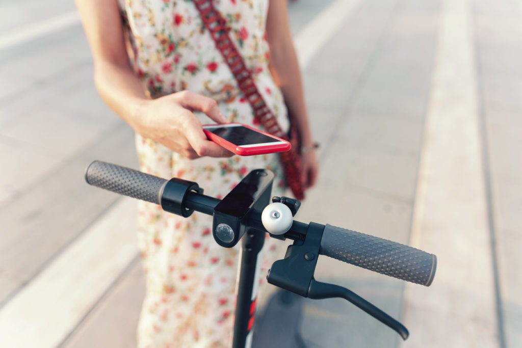 Person tapping their smartphone to a shared e-scooter