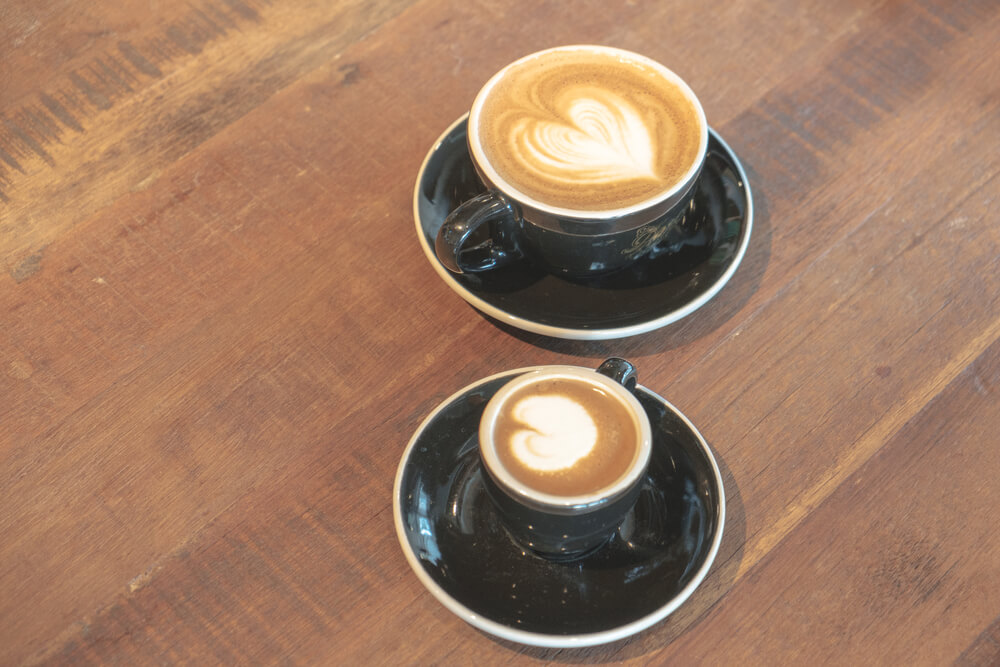Two coffee drinks on a wooden table.