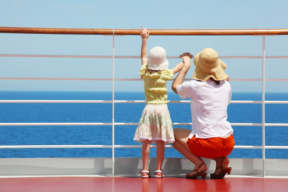 A mom and daughter looking off of the side of a cruise ship.