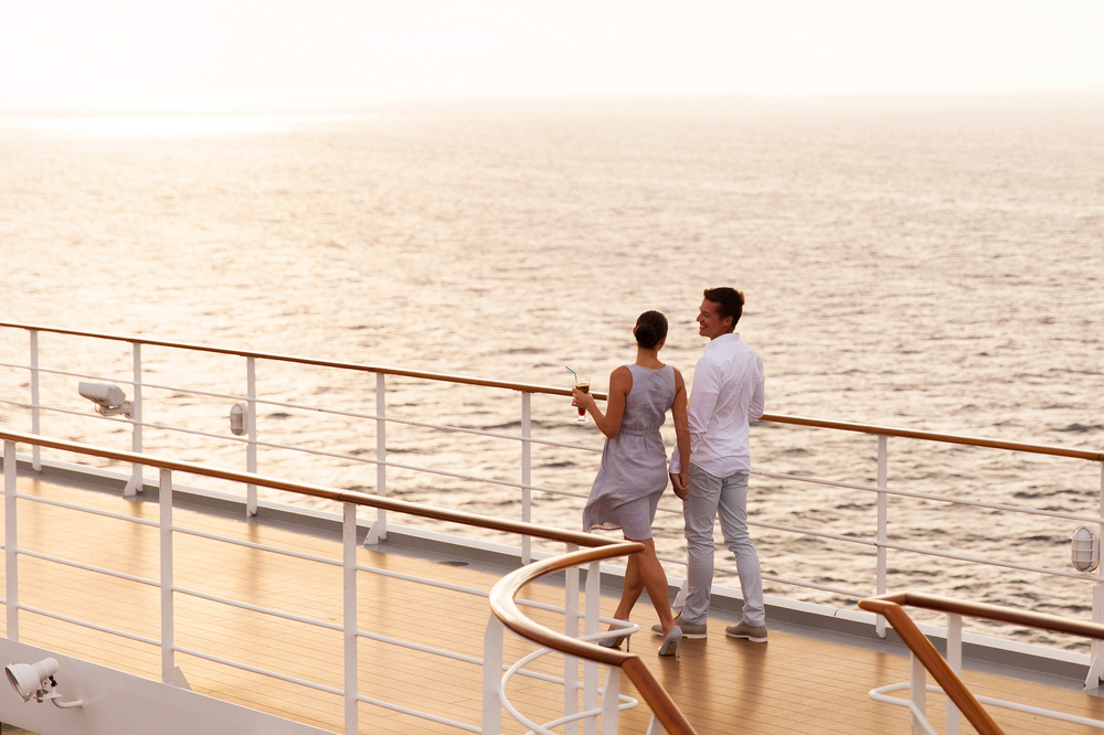 A couple dressed in white on a cruise as the sun sets.
