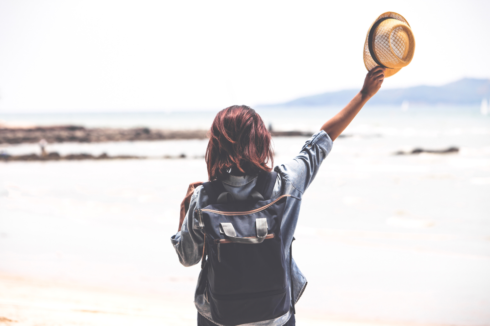 A woman on a beach with a backpack.