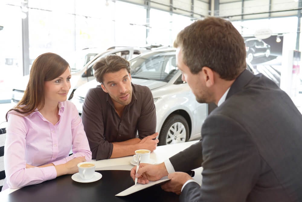 car salesman going over paperwork at dealer with couple