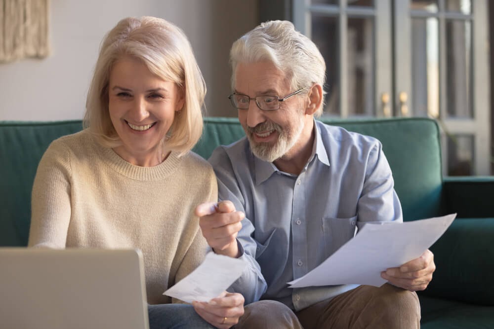 Older couple smiling while looking at laptop and paperwork