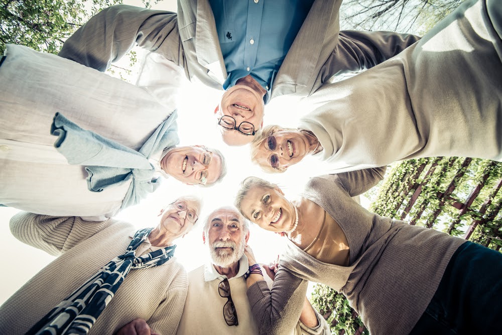 Smiling circle of older people looking down with sun shining through