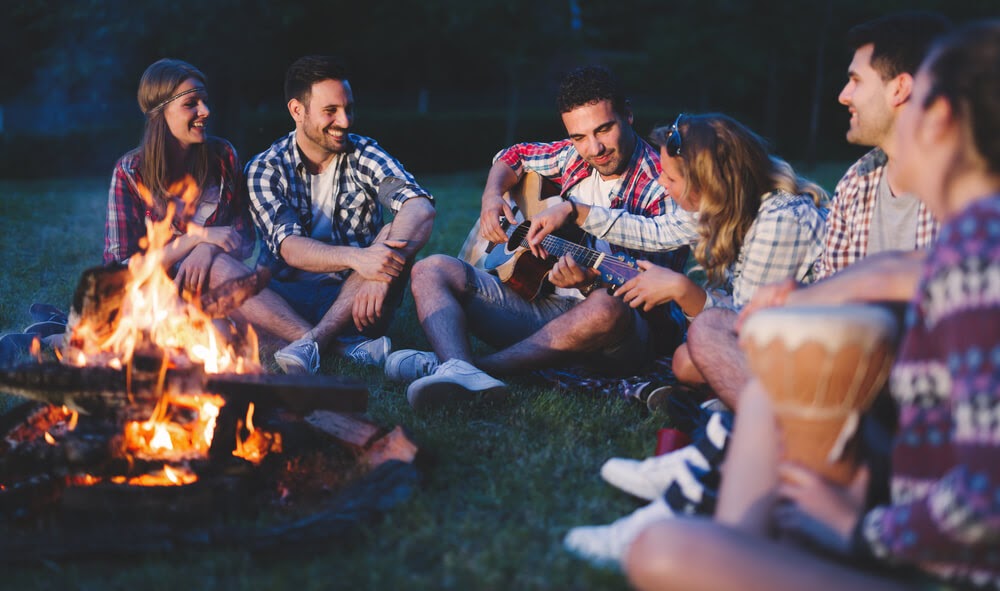 Group of people around a campfire with guitar and drum