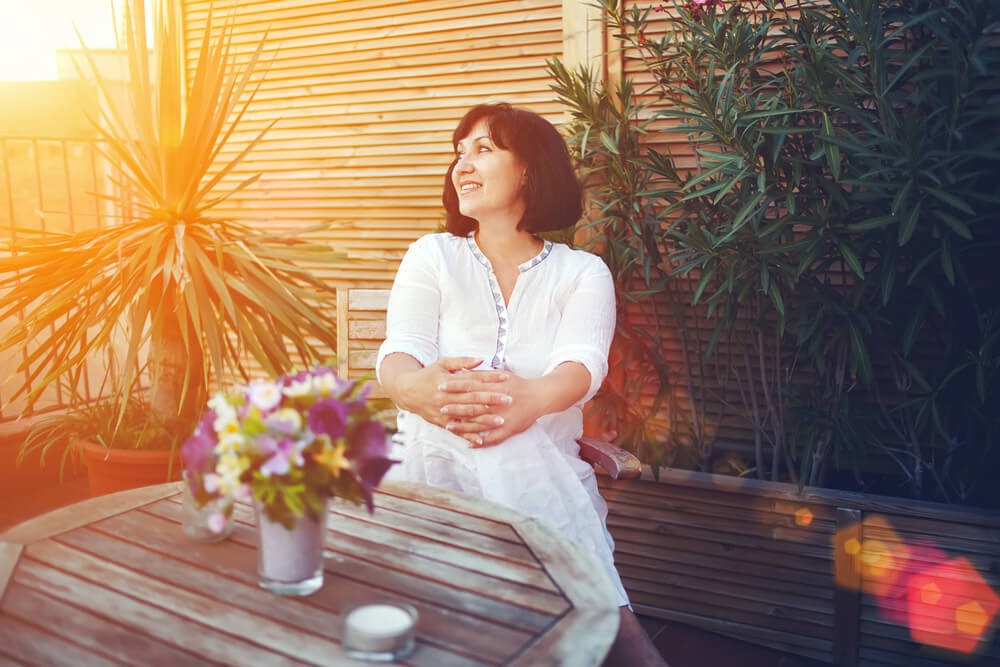 Woman sits on patio at golden hour surrounded by plants