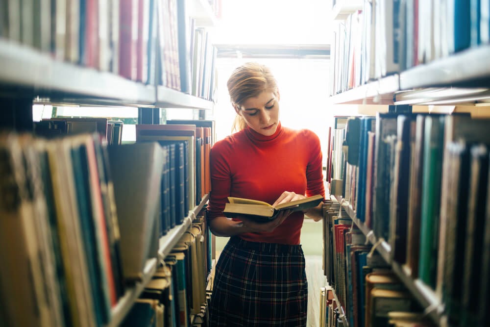 Woman reading book standing in book stacks