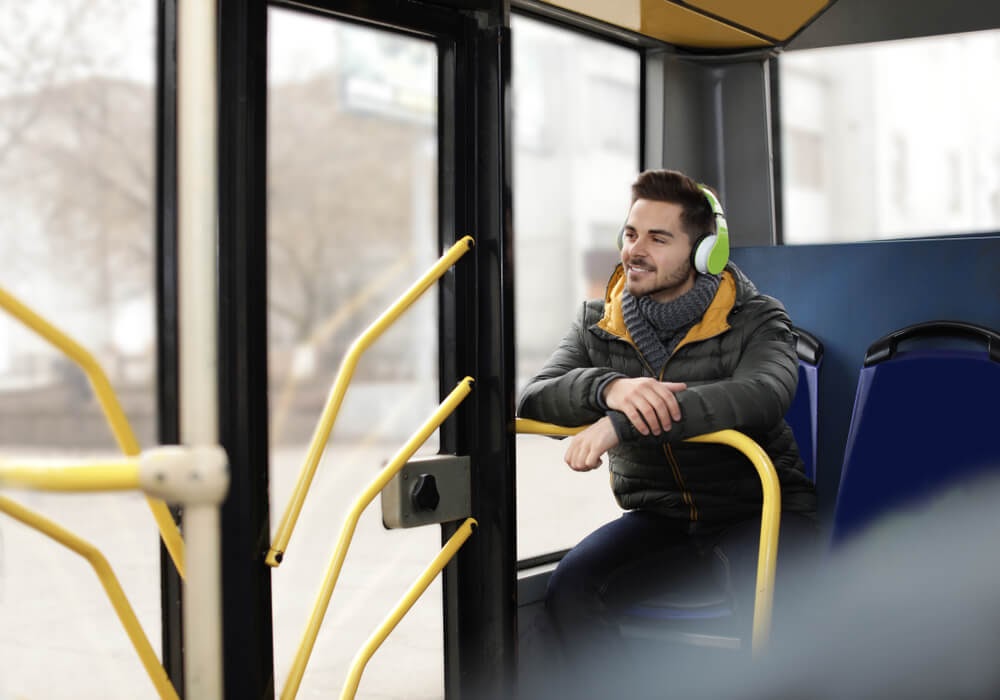 Man sitting on bus wearing headphones and smiling
