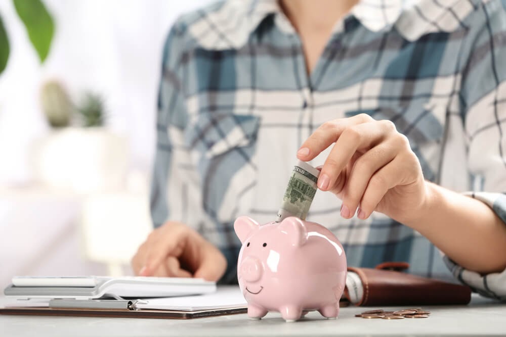 Hand putting money into a pink piggybank.