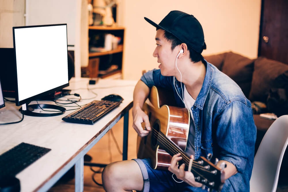 Young man playing guitar and looking at computer screen