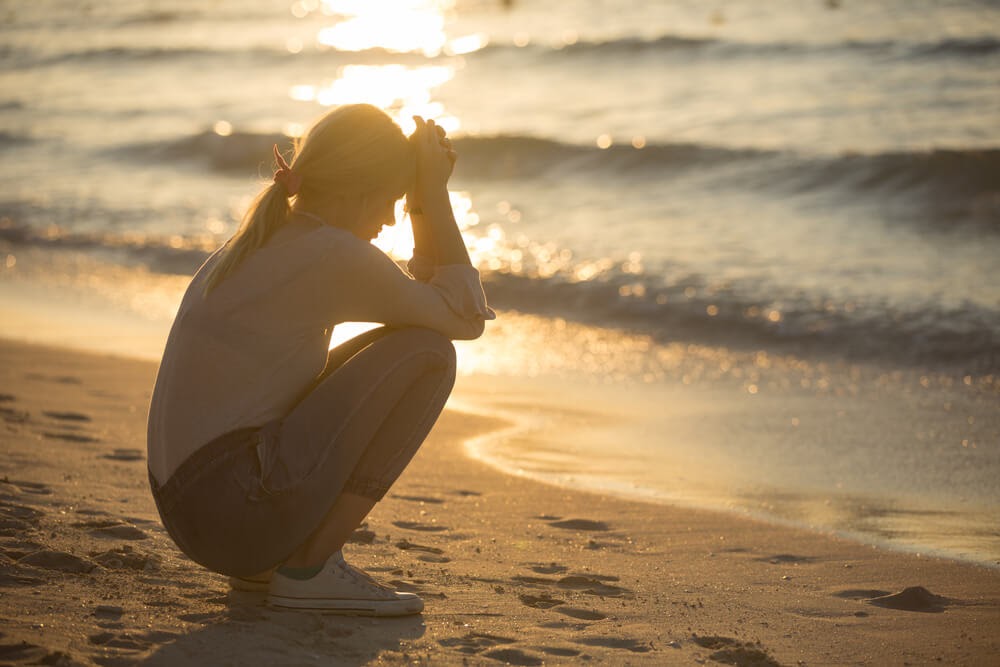Woman kneeling on the beach with head in hands