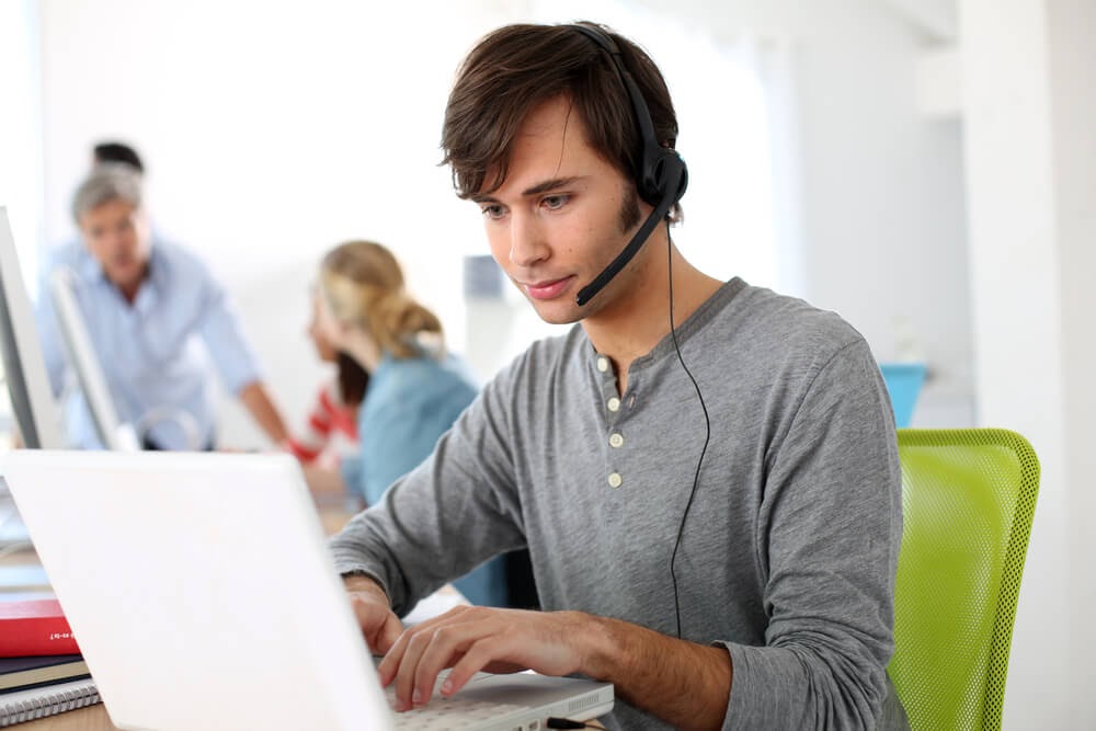 Young man wearning headphones and mic works on laptop