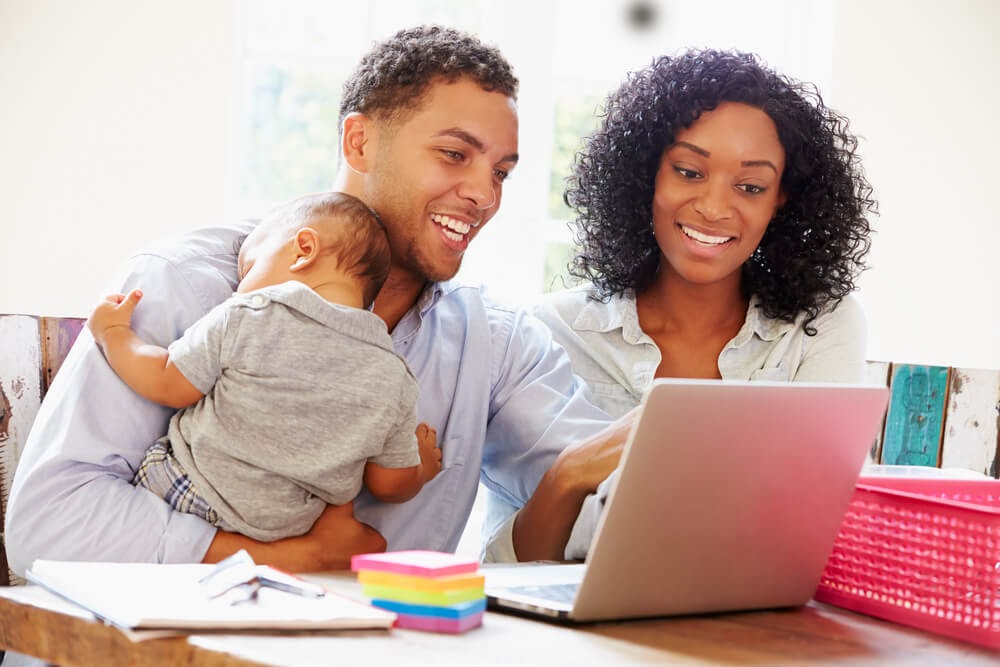 Couple with baby looking at laptop, smiling.