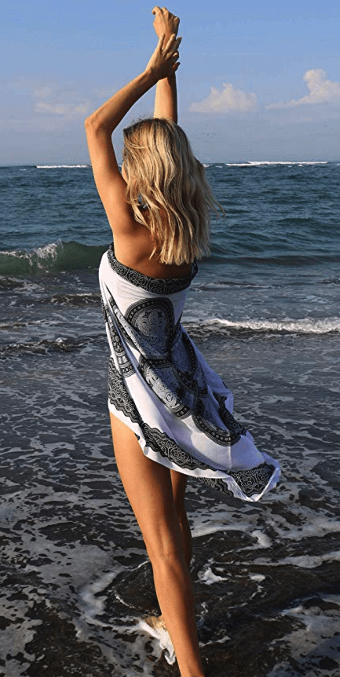 Woman in black and white strapless style sarong wrap stands in front of the ocean.
