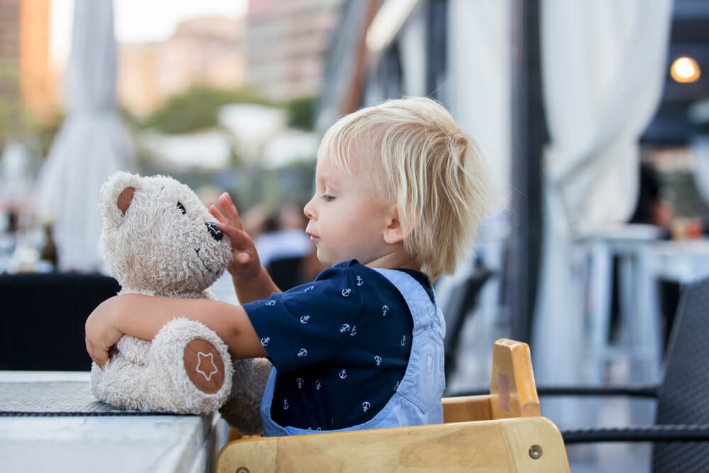 Toddler in restaurant highchair with stuffed bear.