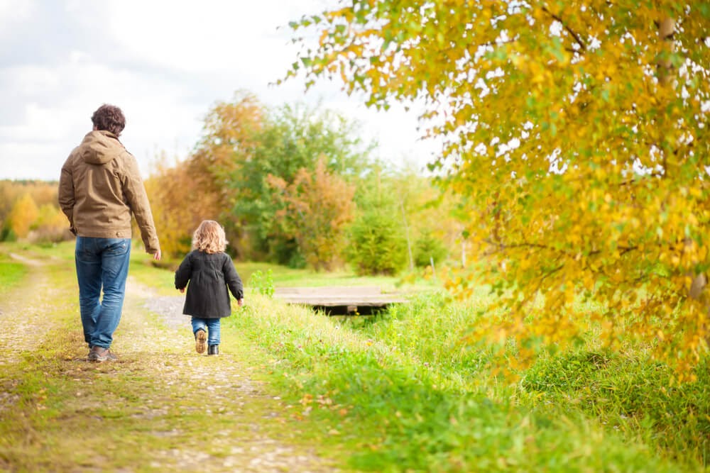 Man and small child walking through yellow and green trees on a grassy path.