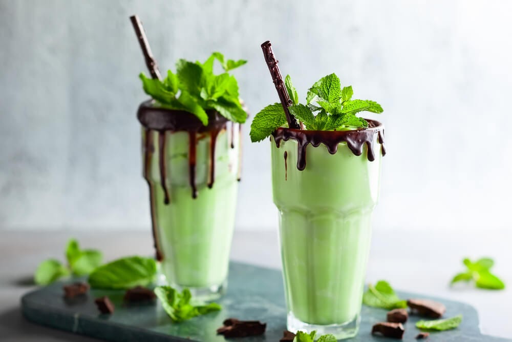 Tall glass filled with green beverage. The rim is drizzled with chocolate and garnished with mint.