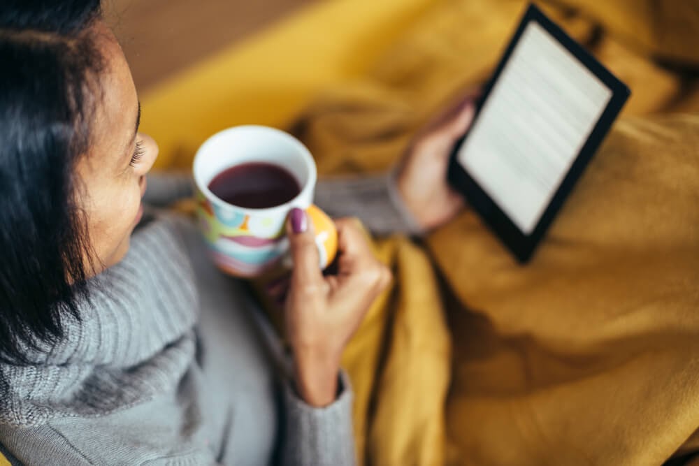 Woman reading tablet and drinking tea or black coffee in a colorful mug.