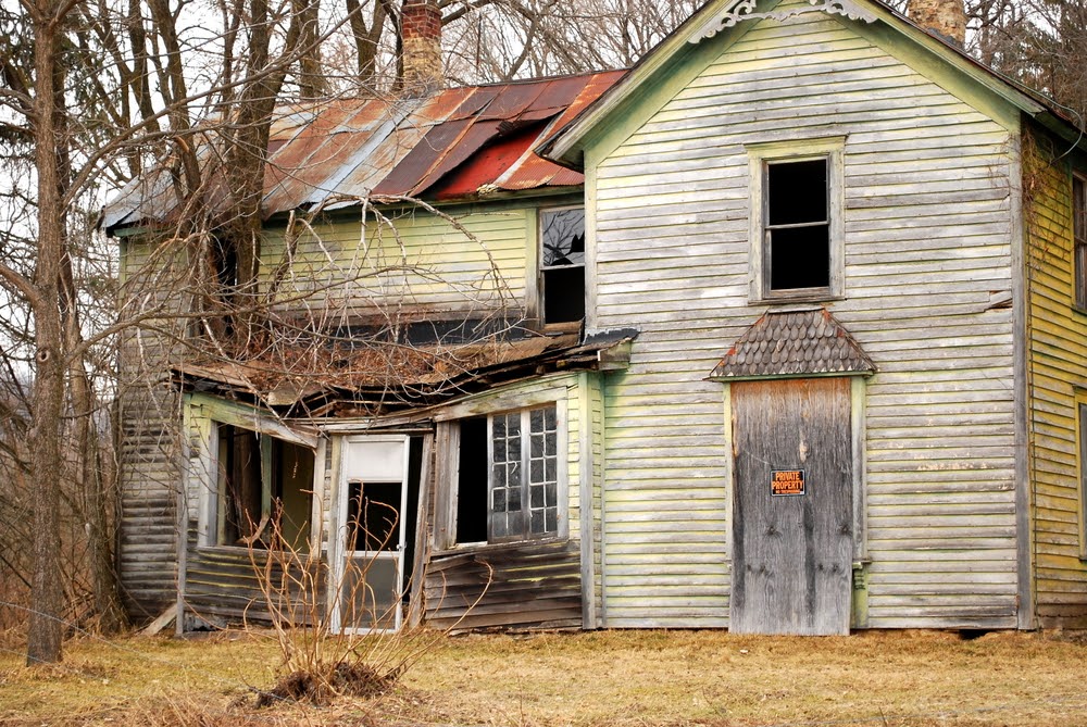 A dilapidated old house with a caved in roof and a private property sign