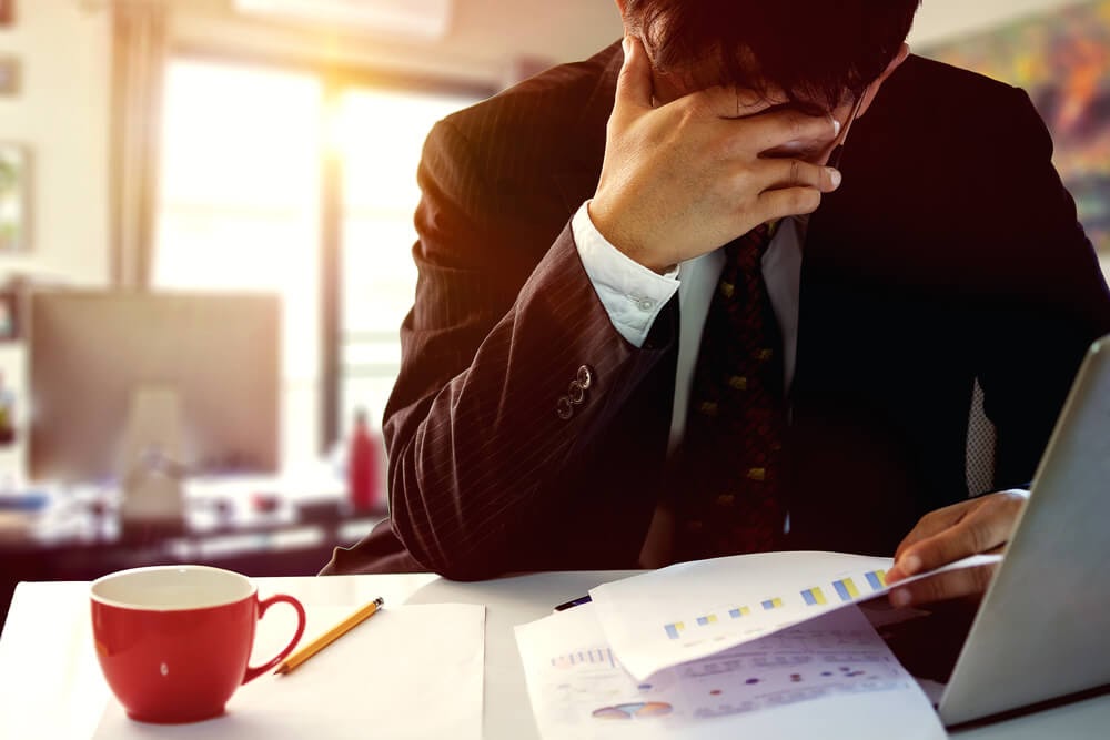 Man working at laptop with his head in his hands.