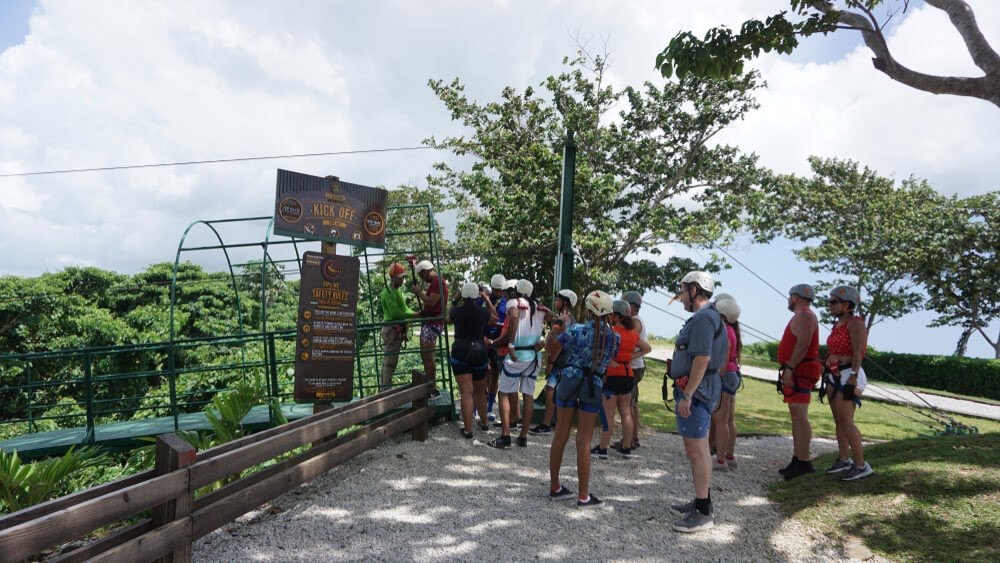 Tourists stand in line with helmets and harnesses on.