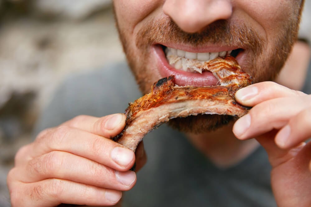 Man taking a bite out of a rib.
