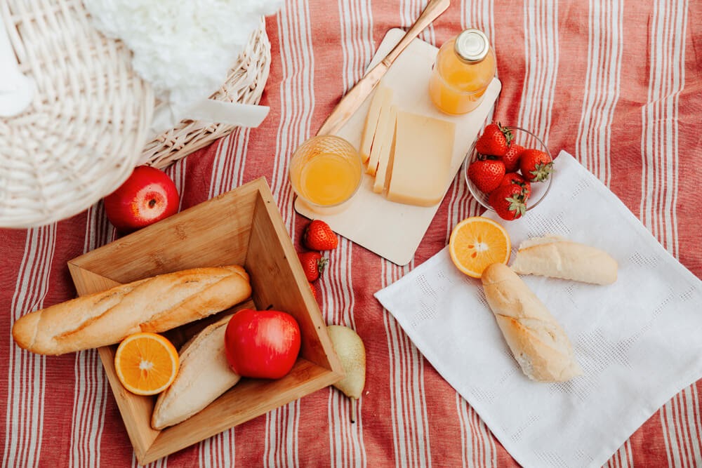 Picnic image with bread, cheese, fruit and juice.