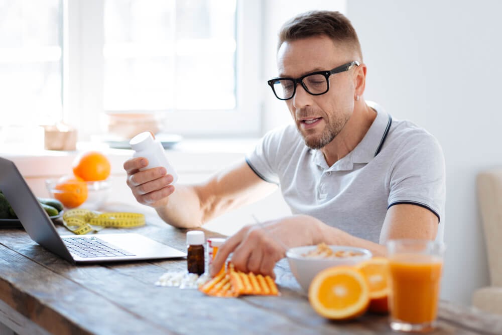 Man looking at pill bottles and a laptop.