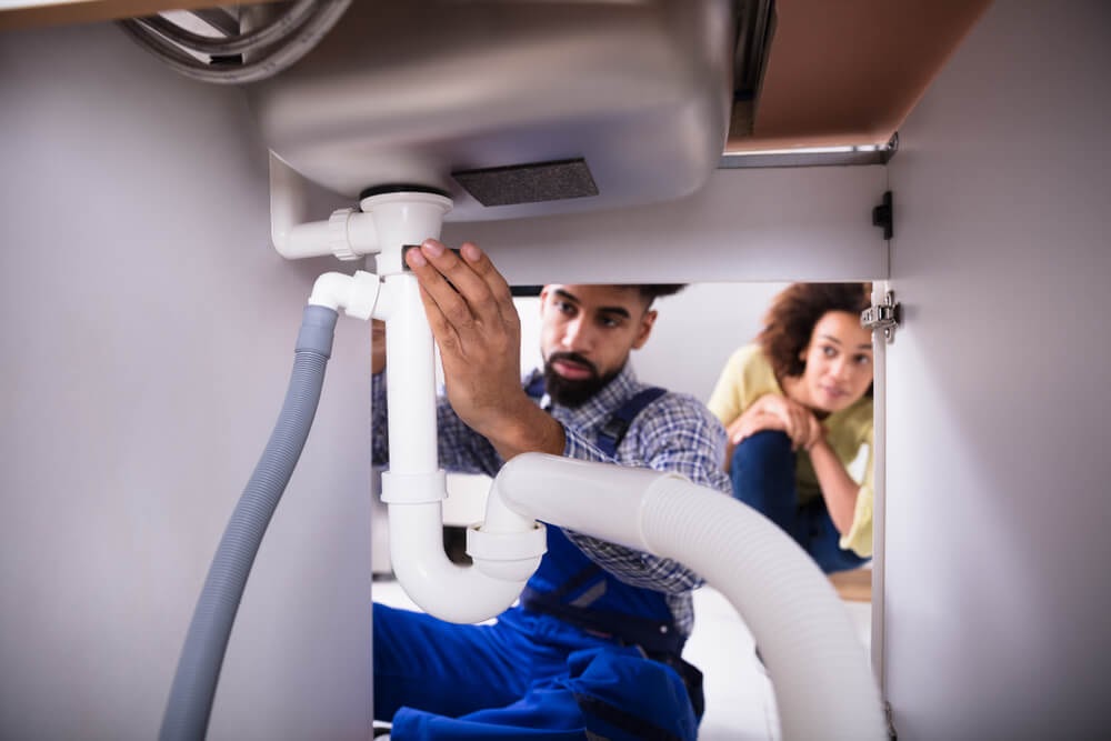 Two people work under the sink.