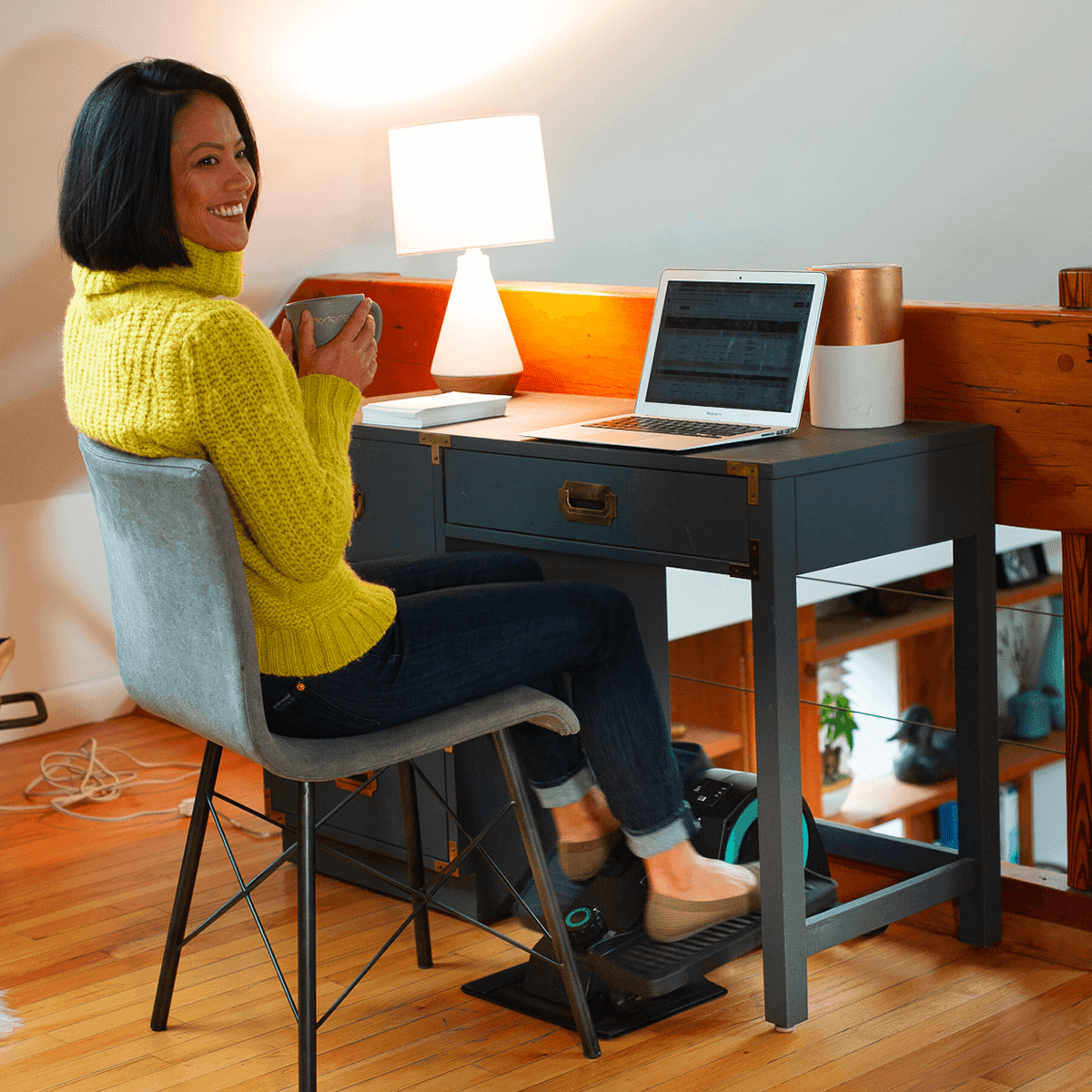 Woman using Cubbi under desk holding a cup.