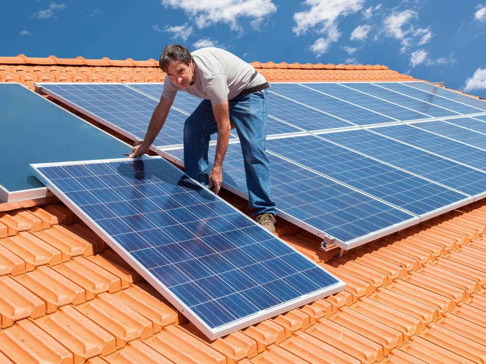 Man on a roof top installing solar panels.