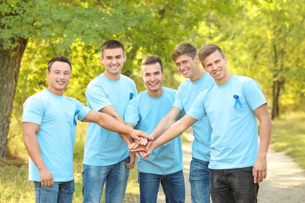 Group of young men all wearing blue shirts with their hands together in a circle.