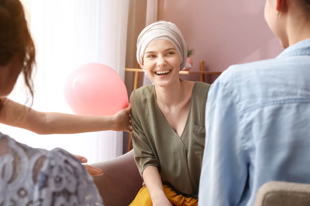 Three people laughing, focus is on young woman with head wrapped.