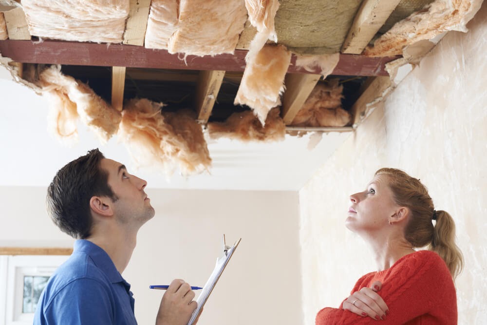 Two people look up at a damaged ceiling.