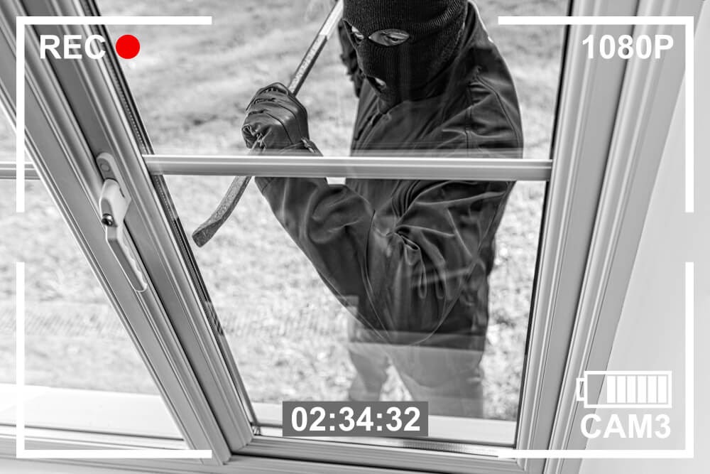 Security footage of a break-in. Perpetrator has on a black ski mask and uses a crowbar.
