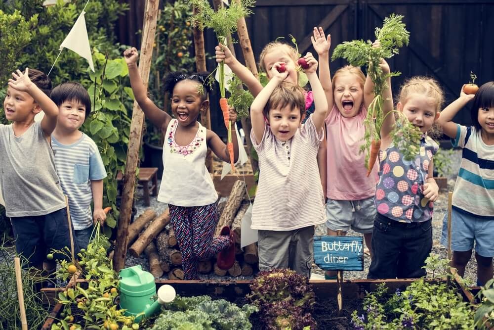 Excited kids hold up plants and vegetables.
