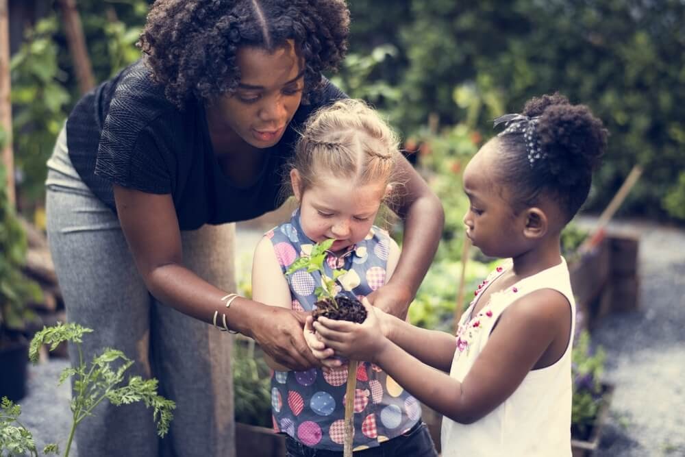 Woman helps two kids with a plant.