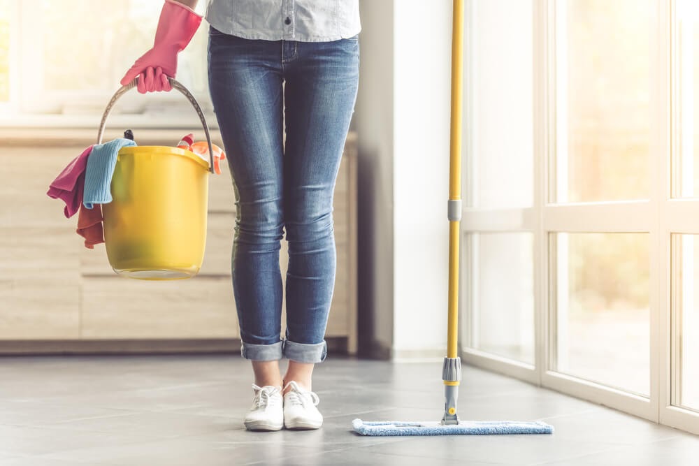 Woman from the waist down holding a mop and a bucket full of cleaning supplies.