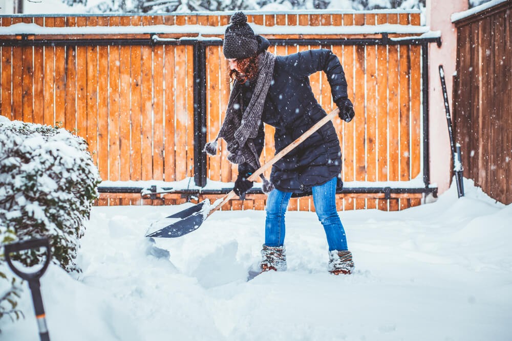 Woman shovels snow during snowfall.