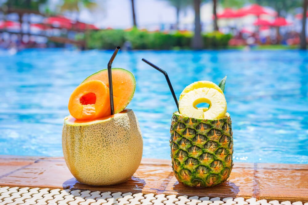 Tropical drinks served poolside in a pineapple and a melon.