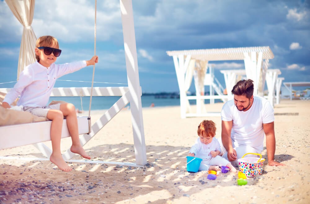 Family all dressed in white play on a white sand beach under a blue sky.