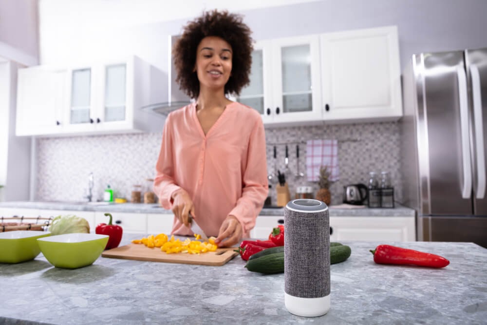 Woman cooking dinner and talking to a smart speaker.