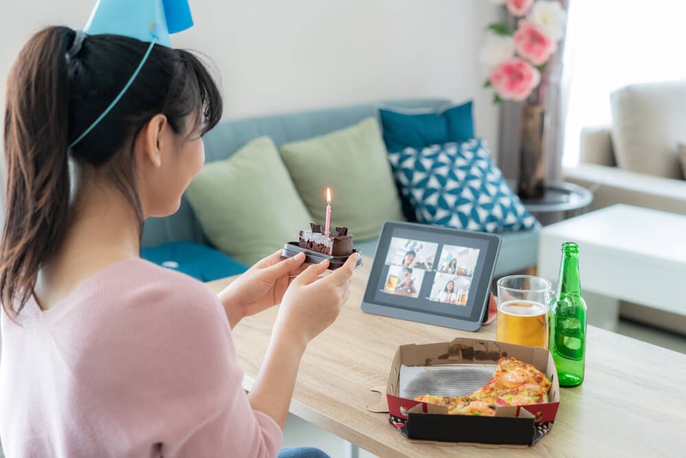 Woman holds single piece of cake up to a video screen and appears to be smiling to four other people.
