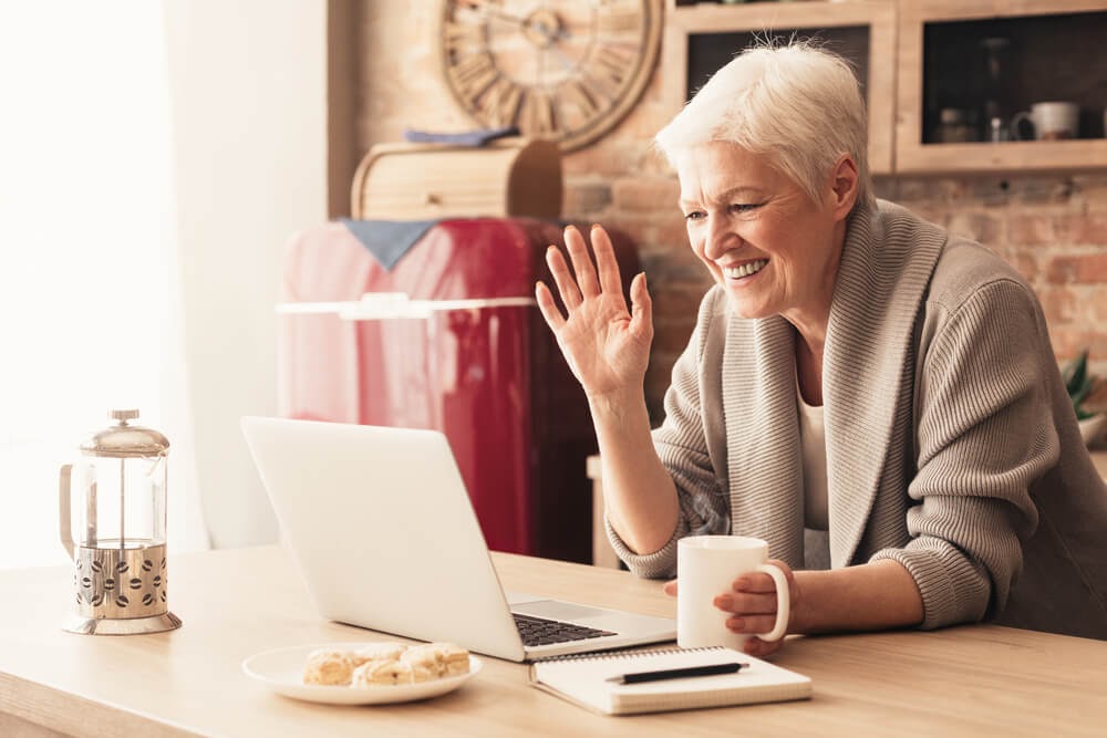Older woman smiles and waves at laptop.