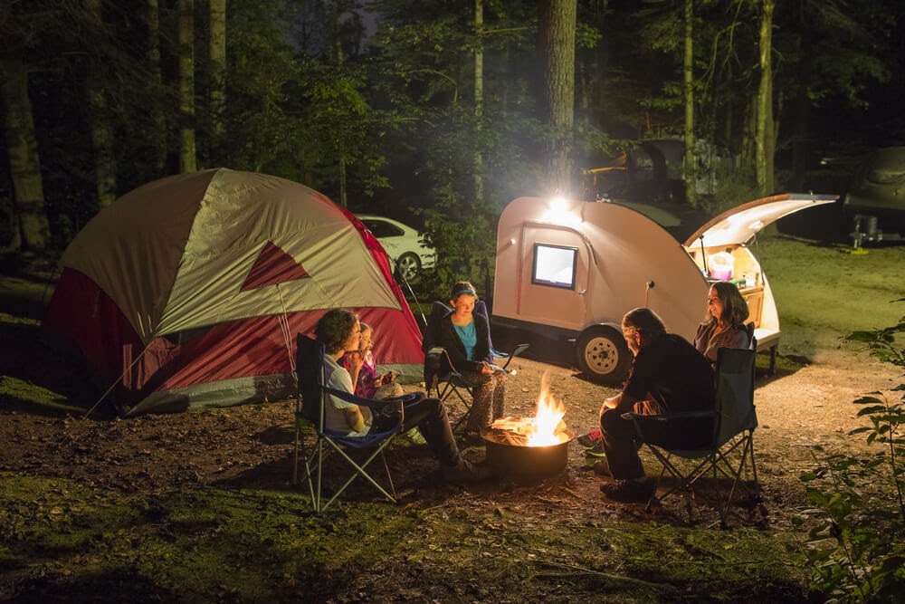 fmaily sits around a campfire with a tent in the background.