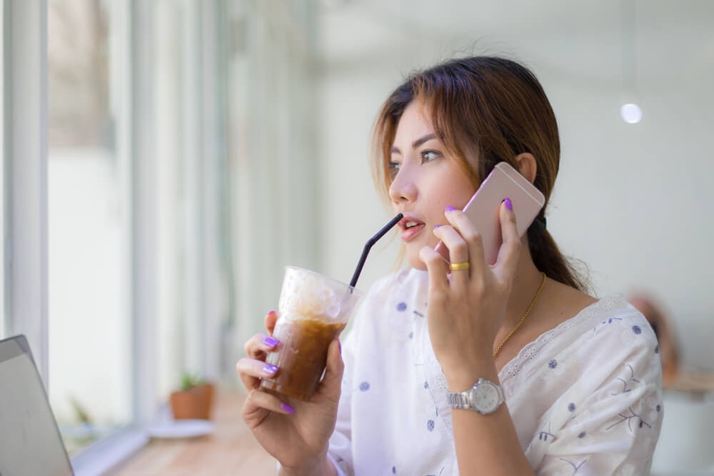 Woman on cell phone drinking cold coffee.