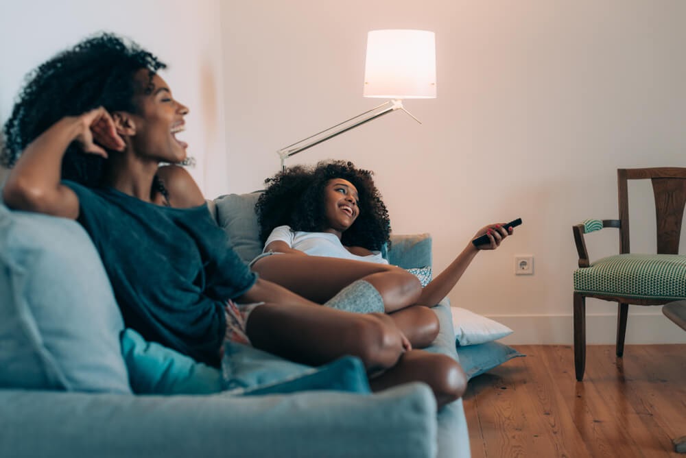 Mother and daughter watch TV on the couch.