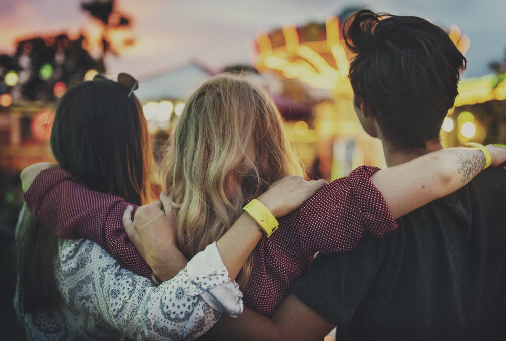 Three people standing with their arms round each other from behind.