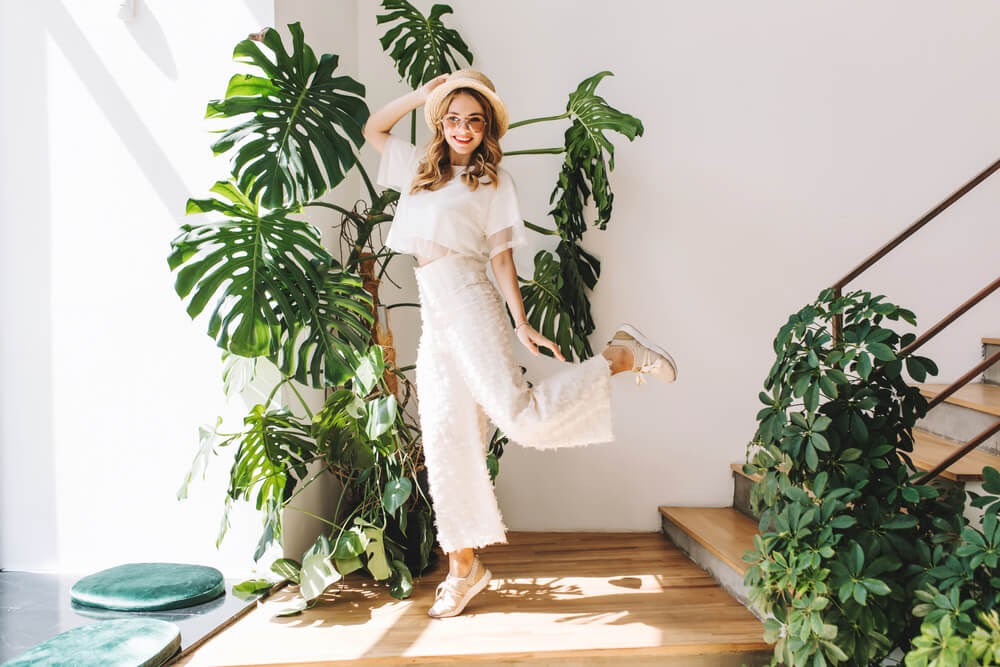 Women dressed in white outfit with hat and sandals. She smiles and poses silly.