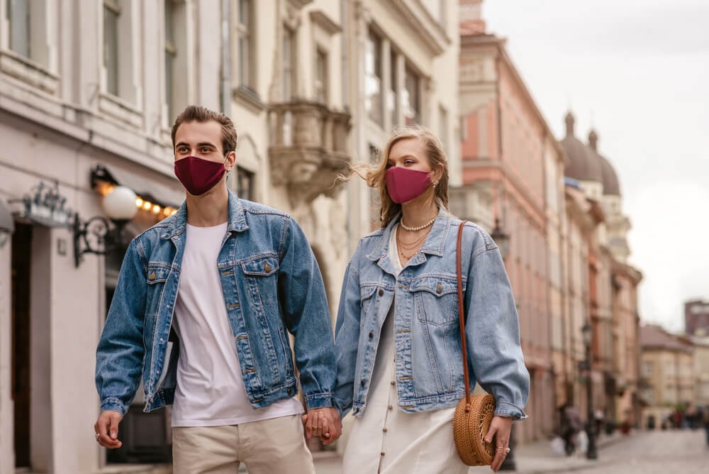 Couple in white outfits and jean jackets. They wear burgundy face masks.